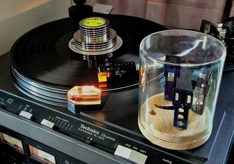 May include: A black Technics Quartz SL-5310 turntable with a record in place. The turntable features a clear protective cover and a wooden base. The controls are visible, and the overall aesthetic is vintage.