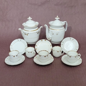 Puede incluir: Un juego de té de porcelana blanca con detalles dorados. El juego incluye una tetera, una jarra de crema, un azucarero y seis tazas y platillos.