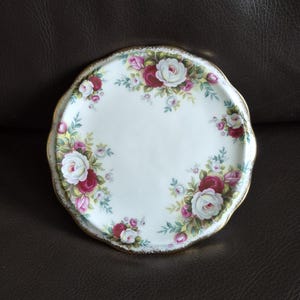 Op de afbeelding: Een witte, geschulpte bord met een bloemenrozenpatroon in tinten rood, roze en wit, geaccentueerd met groene bladeren. Het bord heeft een gouden rand.