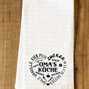 May include: White kitchen towel with a black circle design that says "OMA'S K&Uuml;CHE" with the words "EIER, MEHL, ZUCKER, KEKSE, TORTE, KUCHEN, SALZ, MILCH, BUTTER, BACKEN, VANILLE" surrounding the center text.