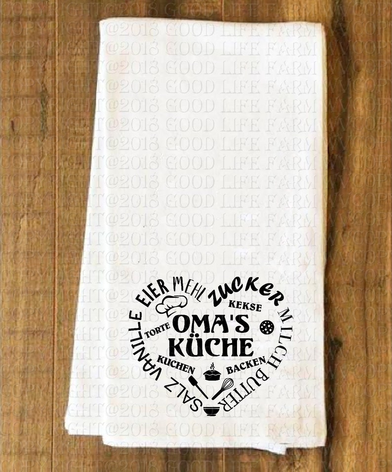 May include: White kitchen towel with a black circle design that says "OMA'S K&Uuml;CHE" with the words "EIER, MEHL, ZUCKER, KEKSE, TORTE, KUCHEN, SALZ, MILCH, BUTTER, BACKEN, VANILLE" surrounding the center text.