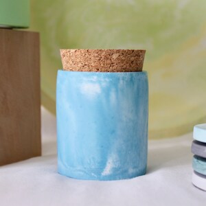 May include: A light blue concrete jar with a cork lid. The jar has a marbled effect with white swirls.