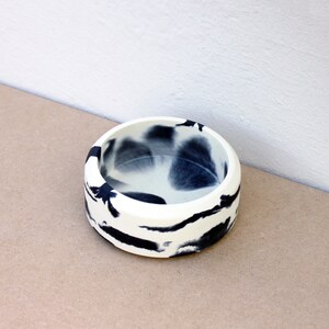 May include: A small, white ceramic bowl with black marbling. The bowl is round and has a smooth, glossy finish.
