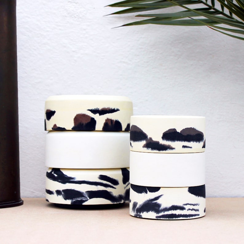 May include: Two sets of stacked white ceramic containers with black and brown abstract patterns. The containers are cylindrical and have a smooth, glossy finish.