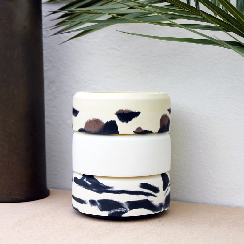 May include: Three stacked ceramic planters with different animal print designs. The top planter has a brown and black leopard print, the middle planter is white, and the bottom planter has a black and white zebra print.