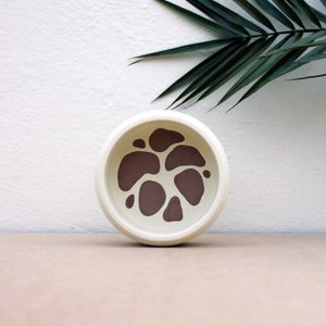 May include: A white ceramic pet bowl with a brown abstract design. The bowl is round and has a smooth, glossy finish.