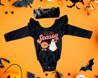 Puede incluir: Mono negro de manga larga con un gráfico de una calabaza y un fantasma con el texto "Tis the Season". El mono tiene una diadema negra con lazo.