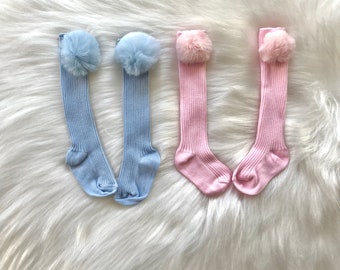 May include: Two pairs of knee-high socks with fluffy pom-poms. One pair is light blue and the other is pink.