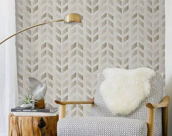 May include: A white and gray chevron patterned wallpaper with a wooden chair with a white faux fur throw pillow and a wooden side table with a book and a potted plant. The chair and table are on a white rug.