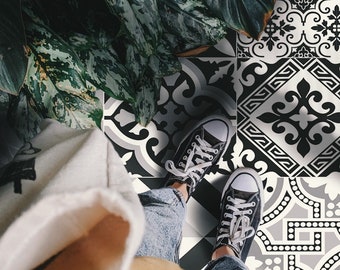 May include: Black and white patterned floor tiles with a person wearing jeans and black sneakers standing on them. A green leafy plant is in the background.