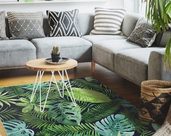 May include: A living room with a gray sectional sofa, a wooden coffee table, and a green and black tropical leaf patterned rug. The room is decorated with plants, a wicker basket, and a white pendant light.