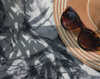 May include: A pair of brown tortoise shell sunglasses with a straw hat on a marble surface with shadows from a plant.