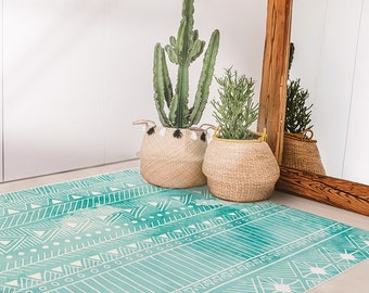 May include: A teal and white patterned rug with geometric designs. The rug is placed in front of a wooden door with a mirror and two potted plants.