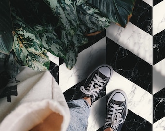 May include: A person wearing black sneakers and blue jeans standing on a black and white checkered floor with a green plant in the background.