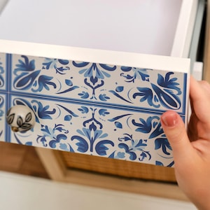 Peut inclure: Tiroir blanc avec un motif floral bleu et blanc. Le bouton du tiroir est un petit bouton rond avec un motif floral. Le tiroir est partiellement ouvert, révélant l'intérieur.