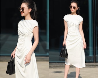 May include: A white midi dress with a gathered waist and short sleeves. The dress is made of a lightweight fabric and has a relaxed fit. The model is wearing the dress with a pair of black sunglasses and a black handbag.