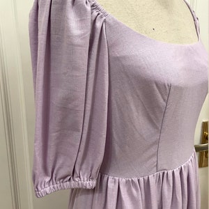 Puede incluir: Un vestido de lino lavanda con escote cuadrado y mangas abullonadas. El vestido tiene un corpi&ntilde;o ajustado y una falda fruncida. El vestido est&aacute; hecho de una tela ligera y transpirable, perfecto para el clima c&aacute;lido.