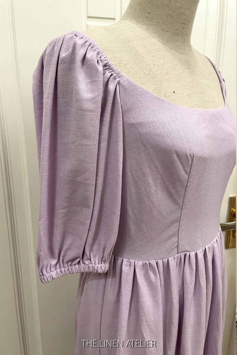 Puede incluir: Un vestido de lino lavanda con escote cuadrado y mangas abullonadas. El vestido tiene un corpi&ntilde;o ajustado y una falda fruncida. El vestido est&aacute; hecho de una tela ligera y transpirable, perfecto para el clima c&aacute;lido.