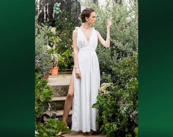 May include: A white linen dress with a V-neckline and a side slit. The dress is photographed in a garden setting.