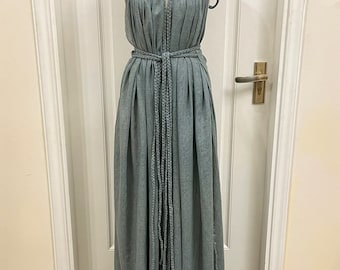 May include: A long, flowing, light blue linen dress with a halter neckline and a rope tie at the waist. The dress has a relaxed, bohemian style.