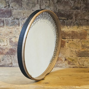 Può includere: Una cornice in legno con un bordo nero e una superficie circolare bianca. La cornice è decorata con un anello di anelli metallici.