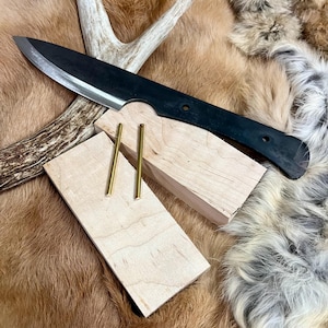 May include: A black knife with a wooden handle is resting on a piece of wood. Two brass rods are also on the wood. The wood is on a brown and white fur.