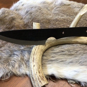 May include: A black knife with a slightly curved blade and a wooden handle. The knife is resting on a piece of antler.
