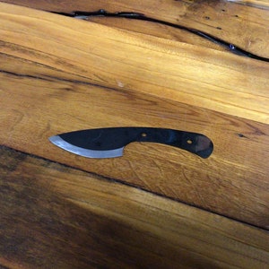 Peut inclure: Une lame de couteau noire avec une poignée incurvée sur une surface en bois.