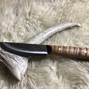 Op de afbeelding: Een mes met een zwart handvat, een gebogen lemmet en een houten handvat met witte accenten. Het mes ligt op een stuk geweihorn.