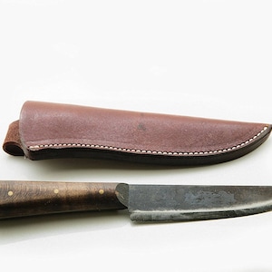 Puede incluir: Una funda de cuero marrón con un borde cosido y un cuchillo de metal oscuro con mango de madera y detalles en latón.