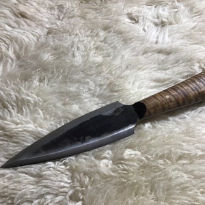 May include: A black-handled knife with a long, pointed blade and a wooden handle with a brown and black wood grain pattern. The handle has two small gold accents.