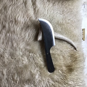 May include: A black, curved knife with a wooden handle, resting on a white, fluffy surface.