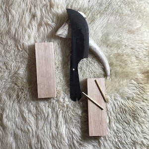 May include: Two wooden blocks with a black knife and two gold metal rods on a white fluffy surface.