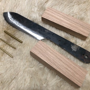 May include: A set of wooden knife handle scales, a metal knife blade, and four brass pins. The knife blade is partially inserted into the handle scales.