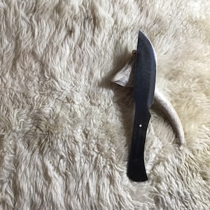 May include: A black handled knife with a silver blade, resting on a white furry surface.