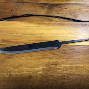 Puede incluir: Una hoja de cuchillo negra con un borde ligeramente curvado, que se encuentra sobre una superficie de madera.