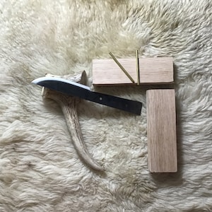 May include: A black knife with a wooden handle rests on a light brown antler. Two wooden blocks with brass pins are also shown.