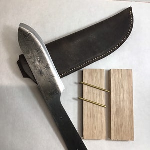 May include: A handmade knife with a black handle and a leather sheath. The knife is resting on a wooden block with two brass pins.