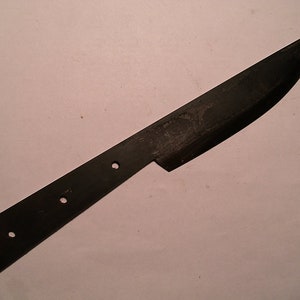 May include: A black metal knife blade with three holes for mounting a handle. The blade is curved and has a sharp point.