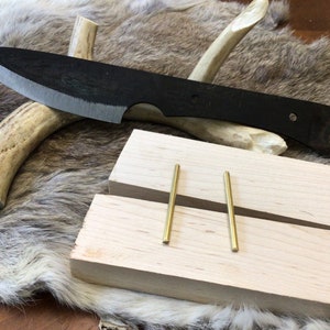 May include: A black knife with a wooden handle is displayed on a white antler. Two brass rods are placed on a wooden block.