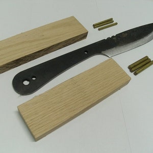May include: Two pieces of wood, one with a darker grain, and a black knife blade with brass pins. The wood pieces are for making a knife handle.