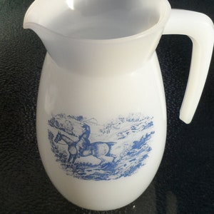 May include: White ceramic jug with a blue and white design of a person riding a horse. The jug has a wide mouth and a handle.