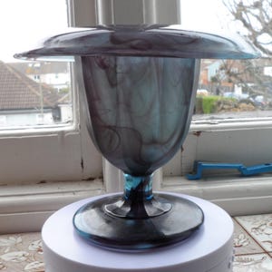 May include: A blue and gray glass vase with a wide, flat top and a swirling pattern. The vase has a tall, slender body and a round base.