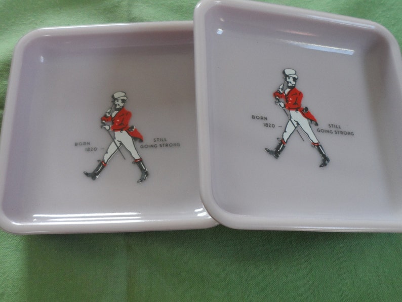 May include: Two square, light purple ceramic ashtrays with a walking man graphic and the text "Born 1820 - Still Going Strong".