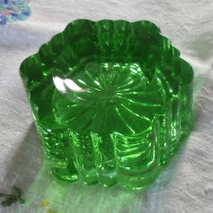 May include: A bright green glass dish with a wavy edge. The dish features a detailed, radial pattern on the inside and a textured exterior. The glass reflects light, creating highlights and shadows. The dish is likely vintage or antique.