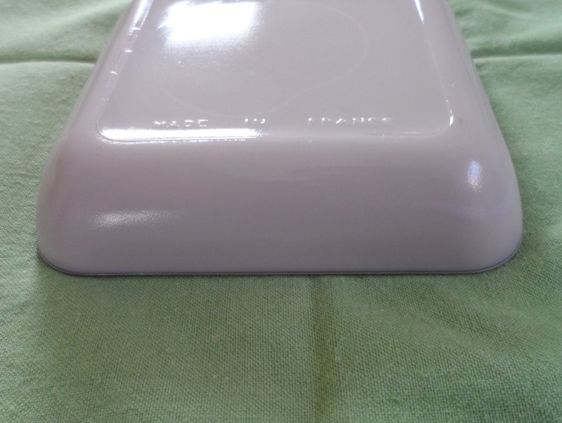 May include: White ceramic baking dish with a gray rim. The bottom of the dish has the words "Made in France" printed on it.