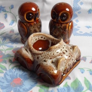 May include: A set of three brown and white ceramic salt and pepper shakers shaped like owls and a car. The owls have brown eyes and a speckled glaze. The car has a brown and white speckled glaze and four wheels.