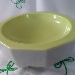 May include: An octagonal ceramic bowl with a pale yellow interior and a white exterior. The bowl has a smooth, glossy finish and a simple, geometric design. Suitable for serving small portions of food or as a decorative item.
