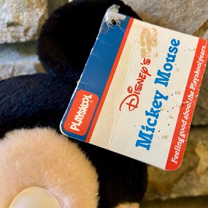 以下が含まれることがあります： ヴィンテージのPlayskoolミッキーマウスのぬいぐるみ。ぬいぐるみは黒い毛並み、クリーム色の顔をしており、青と赤で「Disney's Mickey Mouse」と書かれたタグが付いています。タグには「Feeling good about the Playskool years...」というフレーズも含まれています。