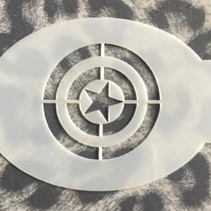 Puede incluir: Plantilla de plástico blanco con un diseño circular que presenta una estrella en el centro. El círculo tiene tres anillos concéntricos alrededor de la estrella.